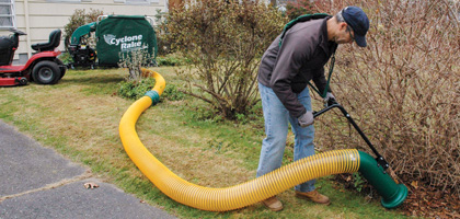 A man using the Estate Vacuum accessory to clear leaves from under a bush.