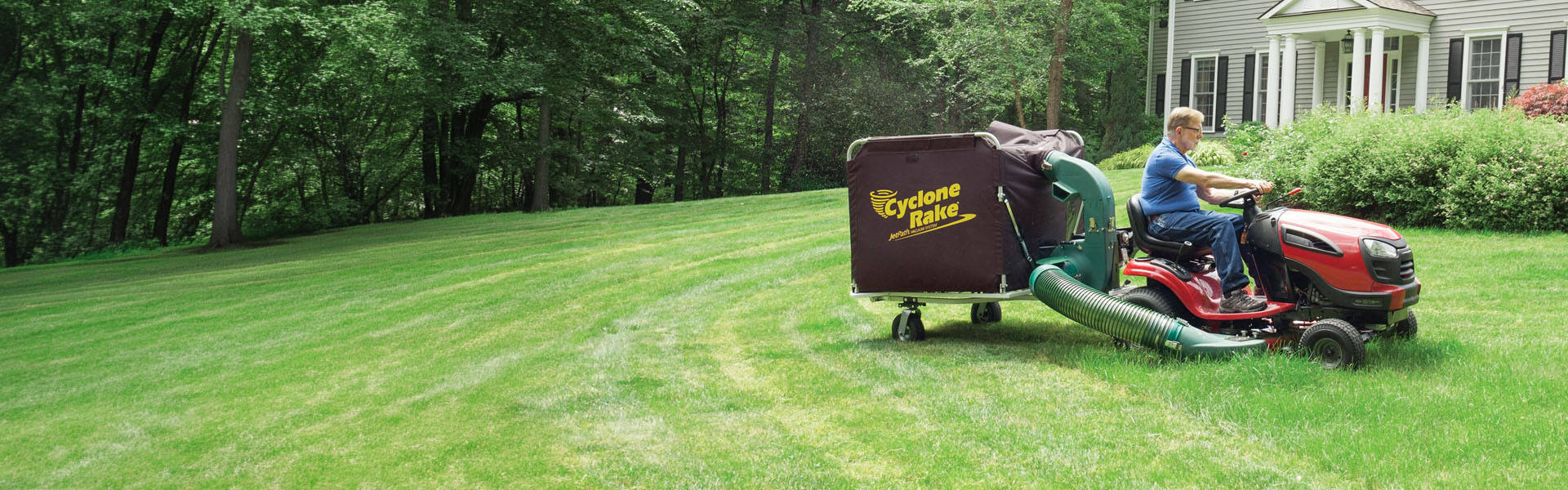 Cyclone Rake lawn and leaf pickup machine being towed by a lawn tractor in a yard in spring