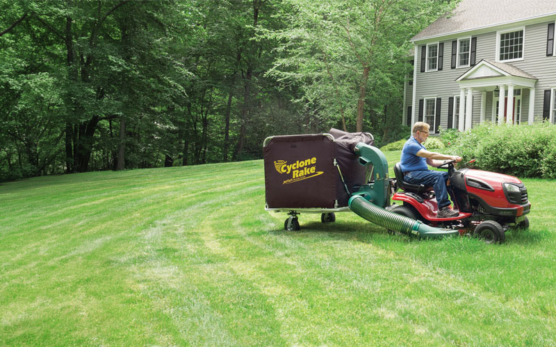 Cyclone Rake lawn and leaf pickup machine being towed by a lawn tractor in a yard in spring
