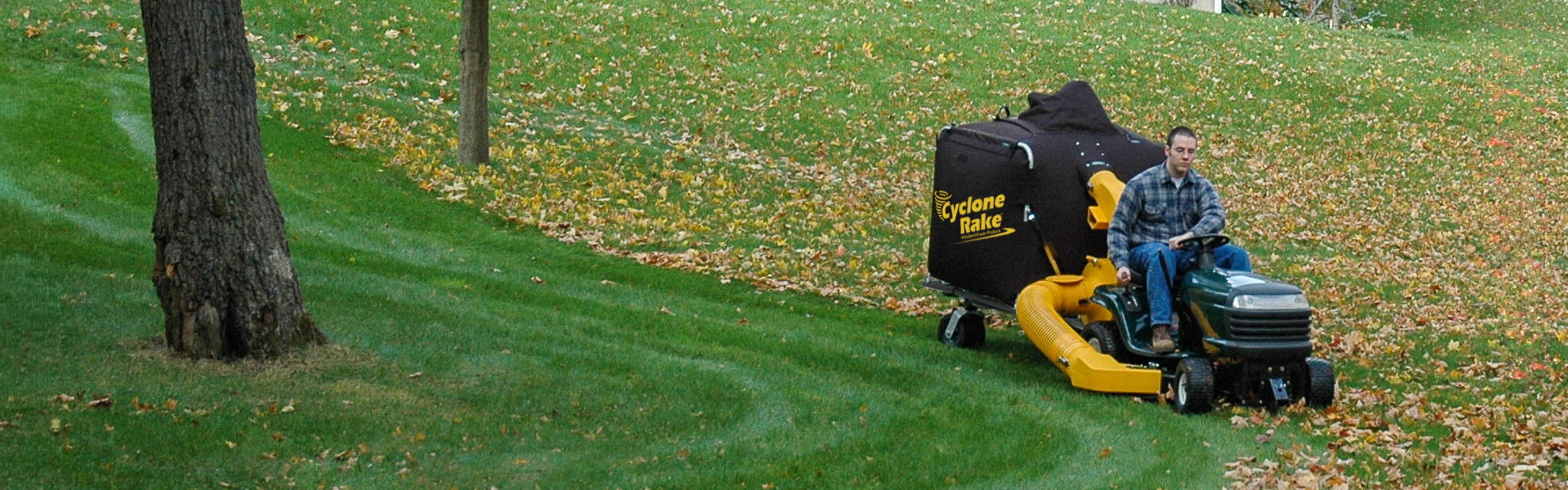 Cyclone Rake XL towed by a lawn tractor across a leaf-covered yard in fall