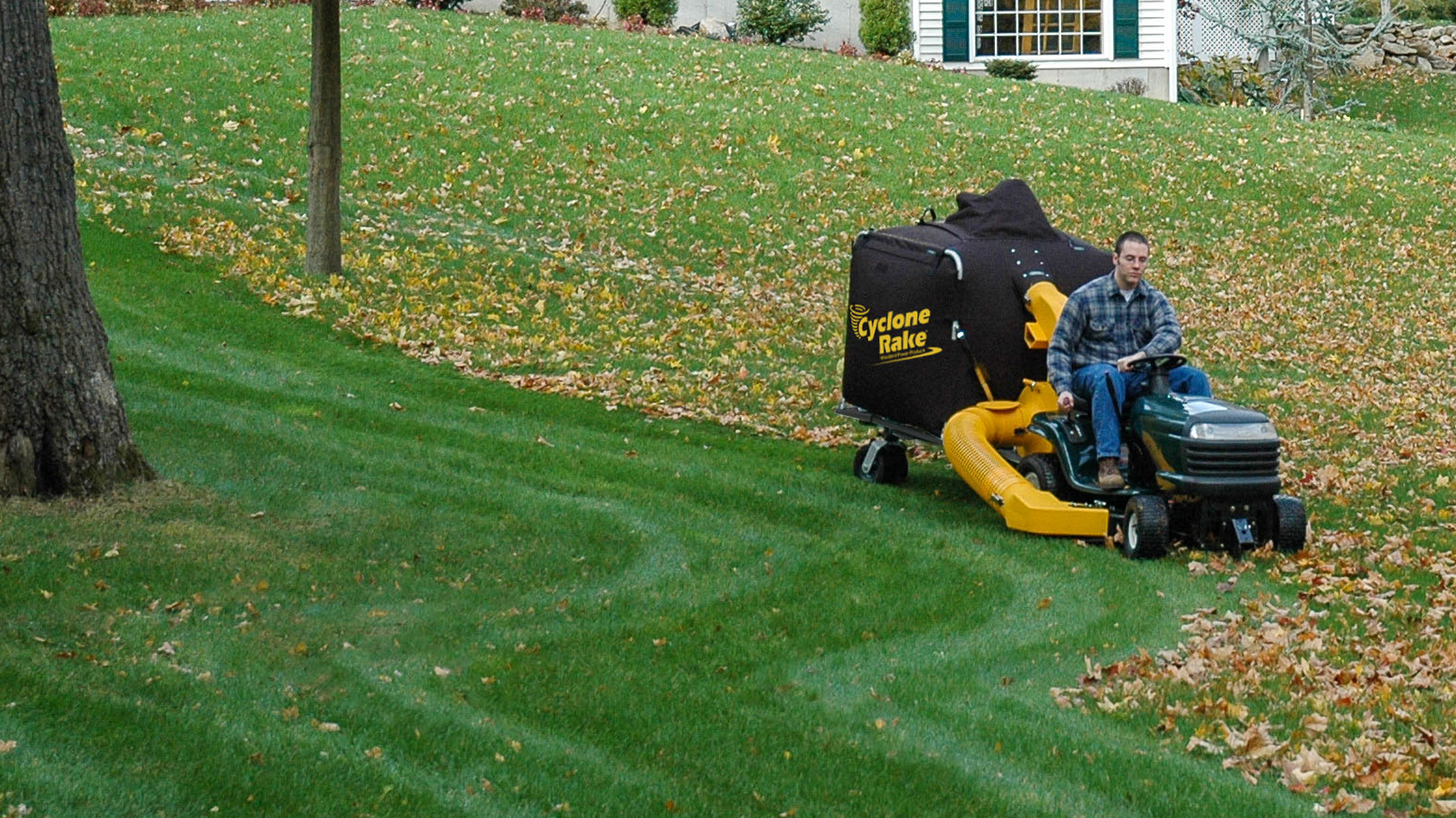 Cyclone Rake XL towed by a lawn tractor across a leaf-covered yard in fall