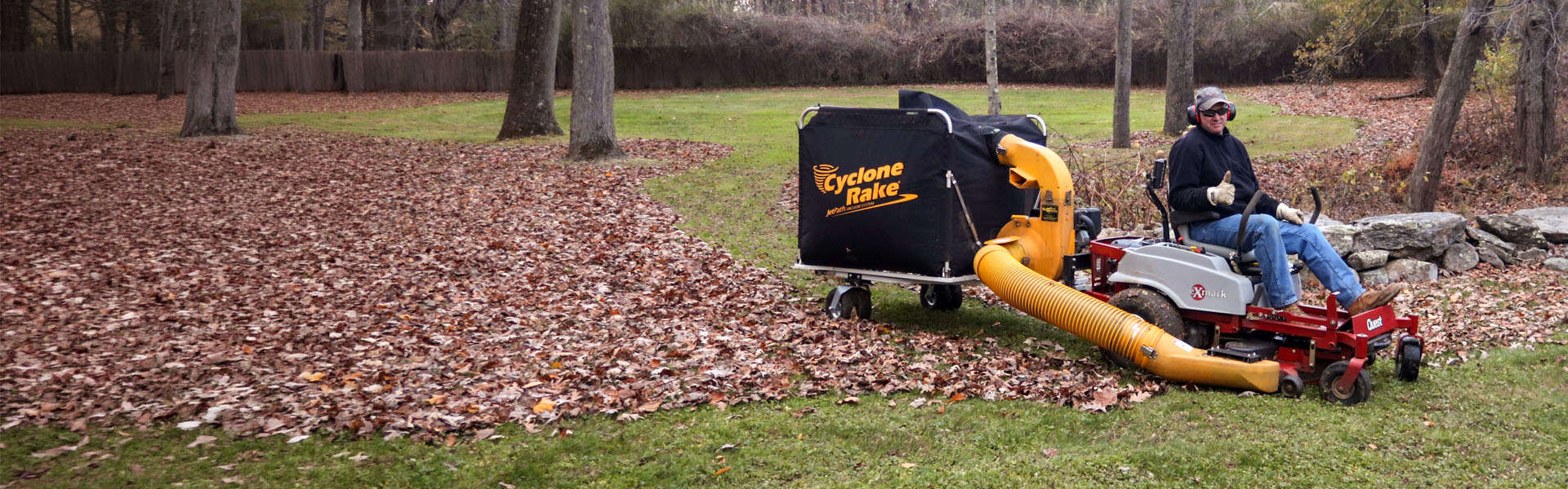 Cyclone Rake XL towed by a lawn tractor across a leaf-covered yard in fall