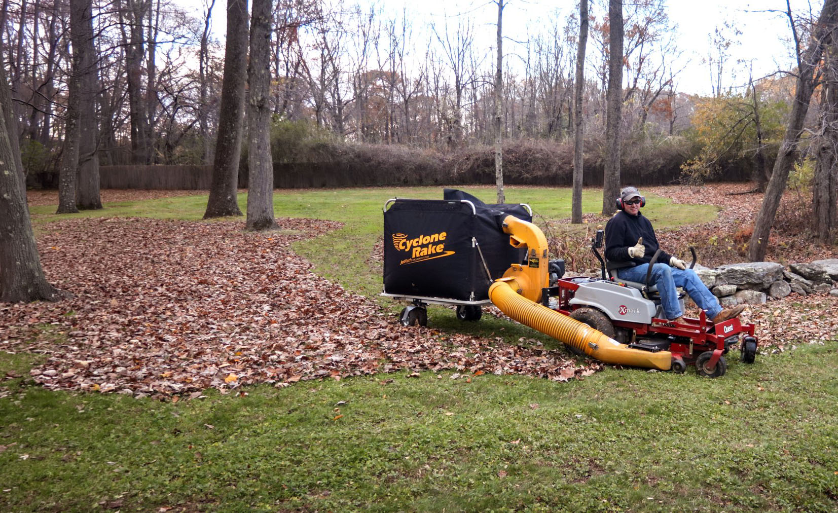 Cyclone Rake XL towed by a lawn tractor across a leaf-covered yard in fall